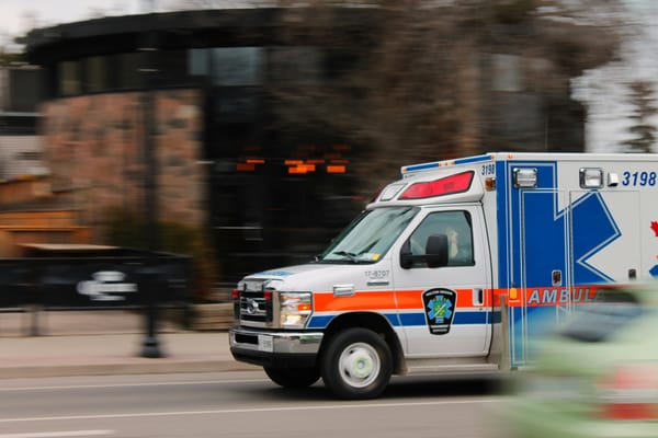 A photograph of an ambulance driving on a road. The background is blurred.